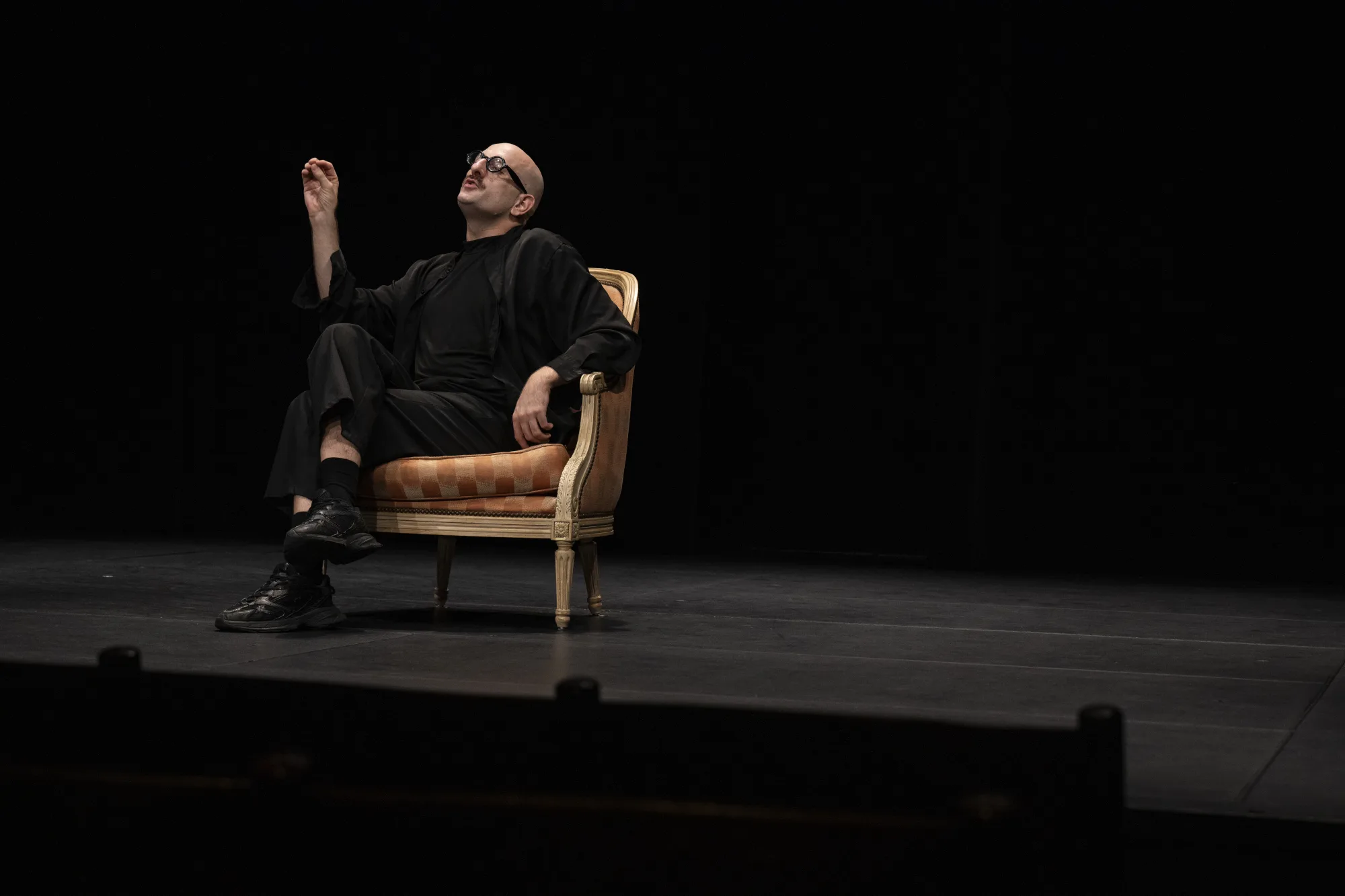Lucas Vuilleumier sur scène, assis dans un fauteuil, pendant Le pédé original